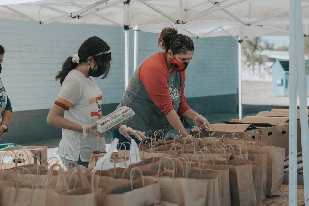 two women packing food in brown paper bags